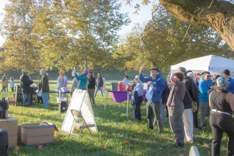 A group gathers around a table with a folding sign in the grass.