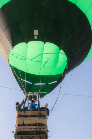 A doodled face design decorates the green balloon fabric against the sky.