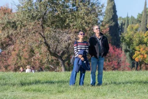 Two guests in scarves and sunglasses stand together on the grass in warm morning light.
