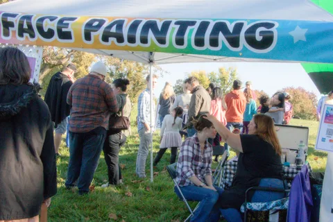 A crowd gathers under a Face Painting tent banner.