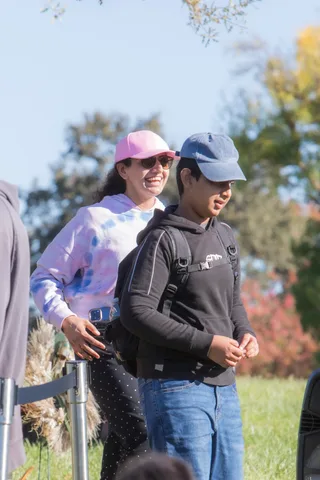 A woman in a pink cap and a man in a dark cap smile together outdoors.
