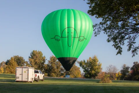 The balloon stands upright on the open field near a parked truck and trailer.