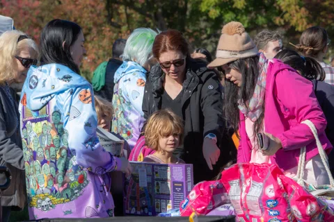 A small crowd gathers at a giveaway table with a child at the center of the group.