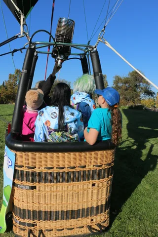 Two riders in colorful jackets are cropped tightly inside a hot air balloon basket.