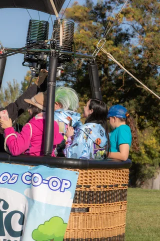 A tightly cropped view of the balloon basket edge with a partial sponsor banner and two riders.