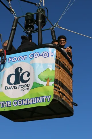 A rider waves from the balloon basket above a Davis Food Co-op sponsor banner.