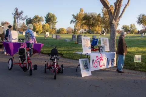 A trike sits parked on the path beside the NorCal Trykers sign as someone walks away.