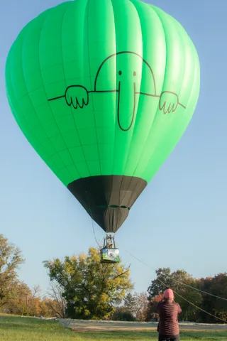 The balloon continues its descent toward the trees as a handler manages the rope.
