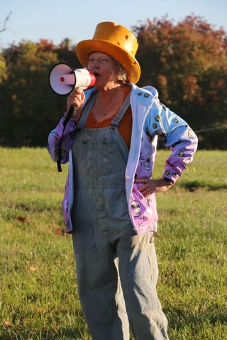 A woman in an orange top hat speaks into a megaphone.