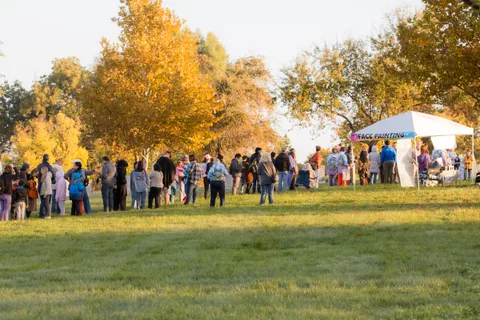 People gather beneath golden autumn trees as the morning light glows behind them.