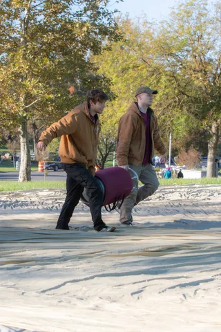 Two crew members carry a rolled purple balloon bag across the pavement.