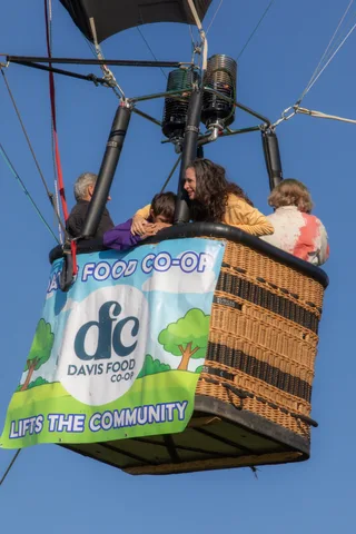 A woman in yellow embraces another rider warmly in the basket.