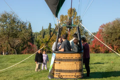 A group of families gathers around the grounded balloon basket on the grass.