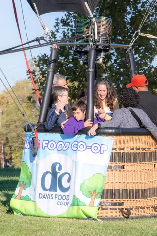 A boy in a purple hoodie peers over the basket rim between two adults.