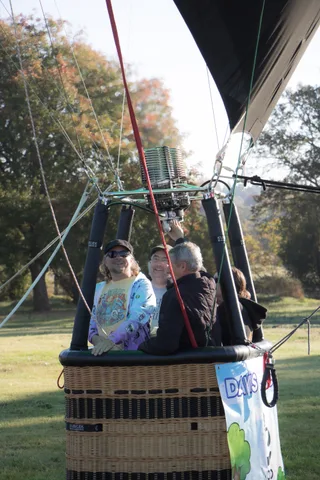 The balloon's burner flares above the basket as two people manage the lines.
