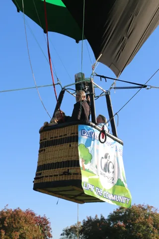 A hot air balloon basket hangs in the sky with a sponsor banner, no people visible.