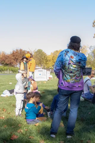 A child in a tie-dye zombie costume stands with a parent near the cemetery headstones.