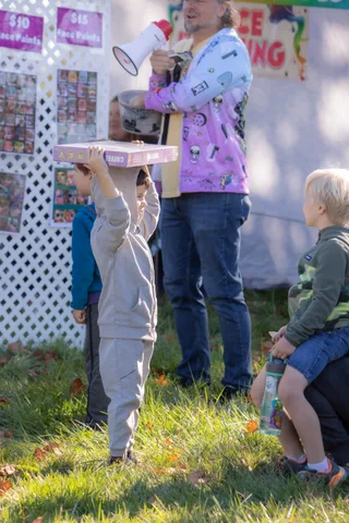 A man speaks into a megaphone near the face painting booth as a child lifts a box.