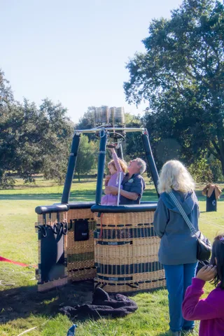 Two women stand and chat near the balloon basket on the ground.
