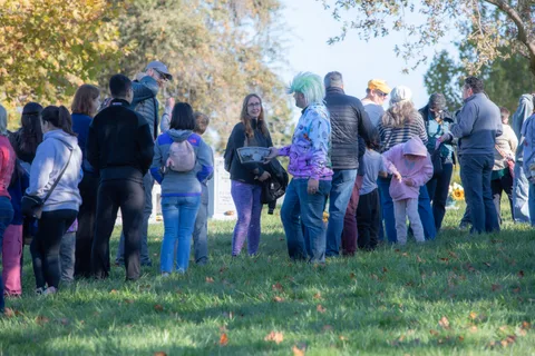 A crowd gathers in the grass field, mostly seen from behind.