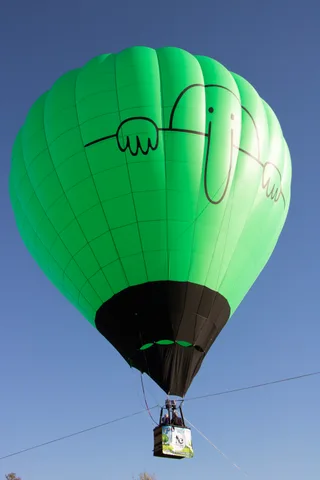 A green hot air balloon painted with a cartoon face fills the frame against a clear sky.
