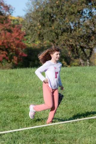 A girl runs through the grass, hair blown back, past a tree turning red for autumn.