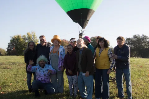 A costumed group poses together in the grass beneath the balloon basket.