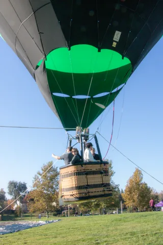 The balloon basket drifts over the open greenbelt with houses and trees spread below.