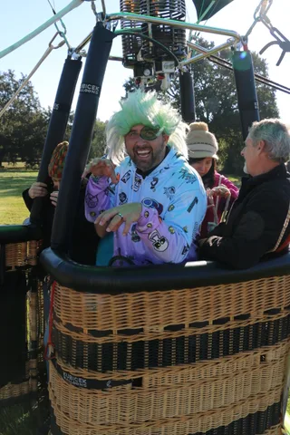 A man in a green wig chats with another rider beneath the balloon burners.