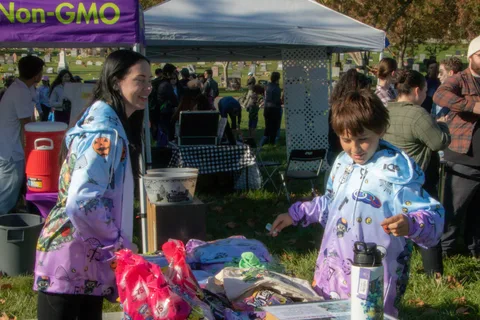 A volunteer in a patterned jacket helps kids at a giveaway table.