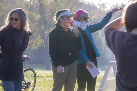 A woman in a pink visor gestures while holding a megaphone beside another woman.