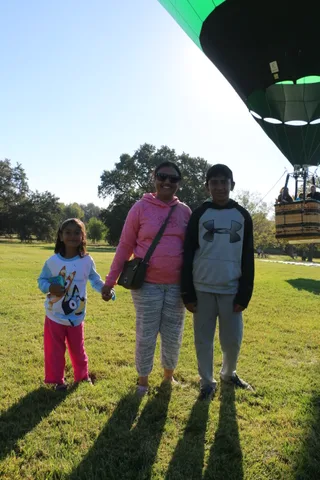 A family stands together on the grass with colorful autumn trees behind them.