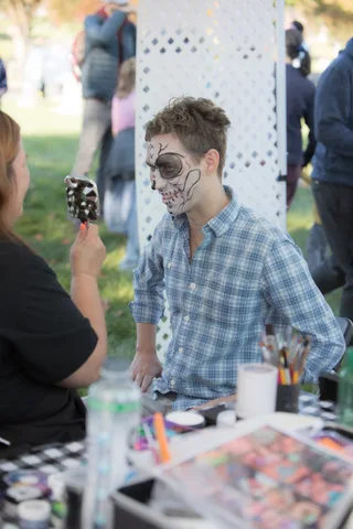A teen shows off dramatic skull and skeleton face paint against a white lattice backdrop.