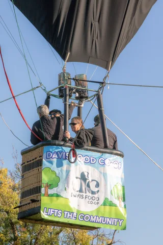 Riders in the balloon basket look out past the Davis Food Co-op banner.