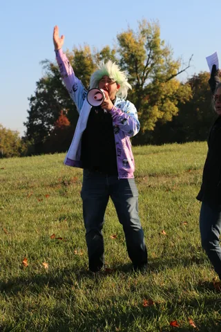 An emcee in a green wig gestures animatedly while addressing the crowd.