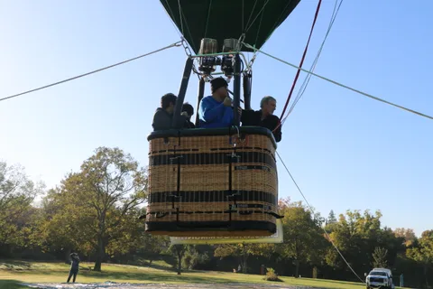 Riders stand in the basket as it lifts off, the co-op banner visible below them.