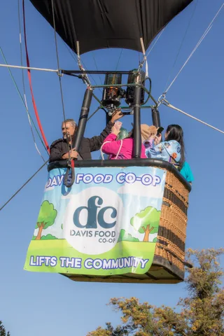 Riders in a hot air balloon basket pose for a photo above a full Davis Food Co-op banner.