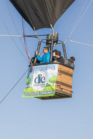 Riders wave from the basket beneath the Davis Food Co-op logo panel.