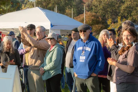 A crowd gathers and claps near a canopy tent at the event.
