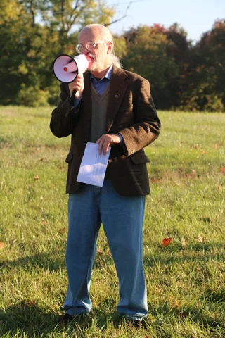 A woman in an orange top hat talks with another attendee on the lawn.