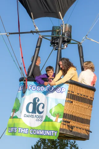 A man and woman lean warmly toward a boy in the basket in bright sun.