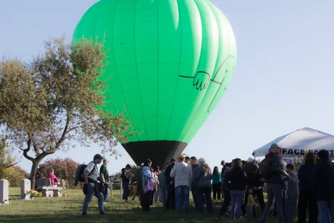 A green hot air balloon descends near the ground as a crowd gathers to watch.
