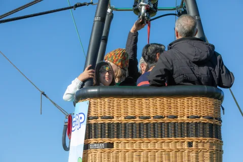 Riders lean over the edge of a hot air balloon basket high above the park.