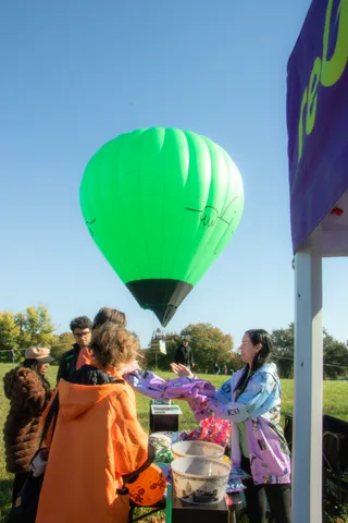 A costumed volunteer hands out treats at a booth with a green hot air balloon floating behind her.