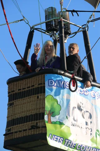 The Davis Food Co-op banner hangs on the balloon basket against blue sky.