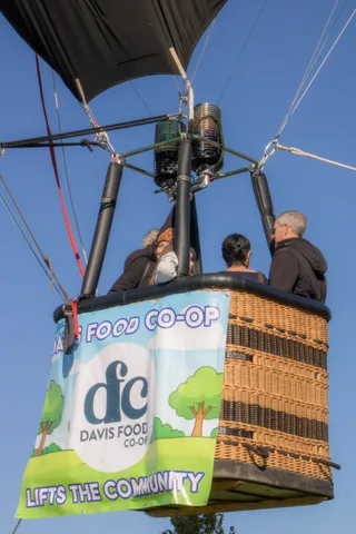 A man's face is barely visible over the rim of a balloon basket wrapped in a Davis Food Co-op banner.
