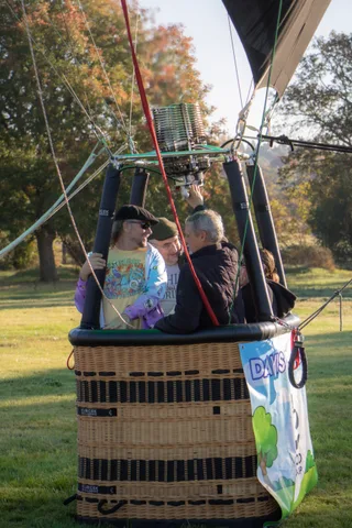 The balloon burner ignites above the basket as two people steady the lines below.