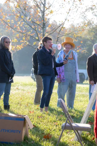 Two people's legs stand near a cardboard box and folding chair in the grass.