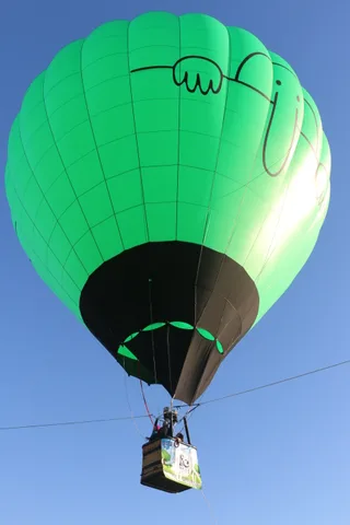 The balloon rises with its basket small against the sky.
