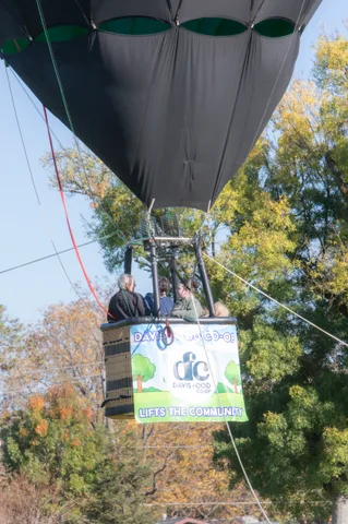 Riders lean over the edge of a hot air balloon basket bearing a full Davis Food Co-op banner.